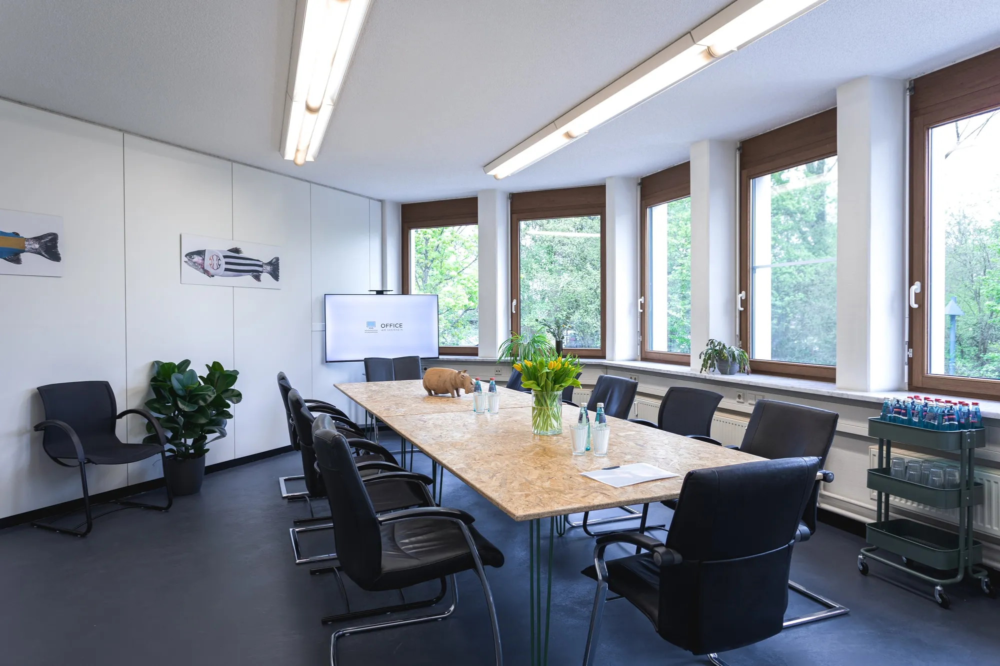 Besprechungsraum mit langem Tisch, Bildschirm und Fensterfront ins Grüne